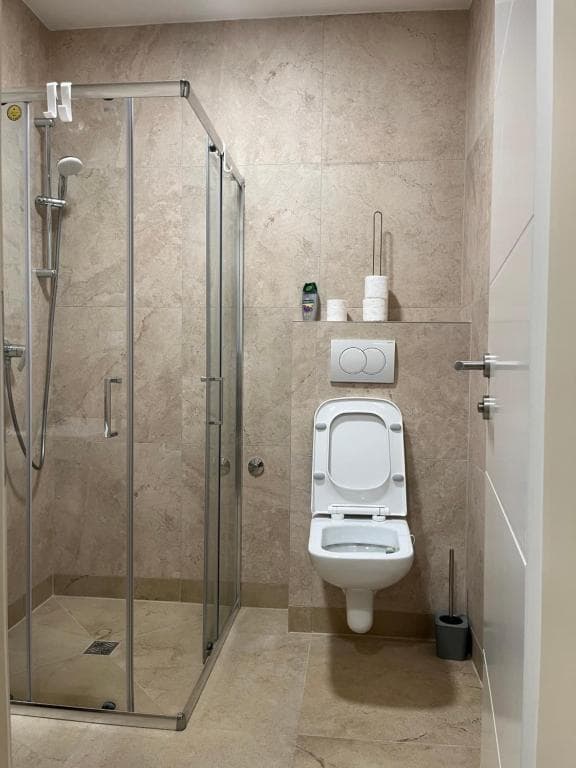 Contemporary bathroom with glass shower enclosure, wall-hung toilet, and light stone-look tiles.