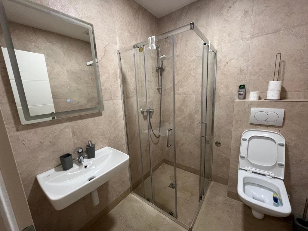 Bathroom with LED-lit mirror, wall-hung basin, glass shower, and coordinated neutral finishes.