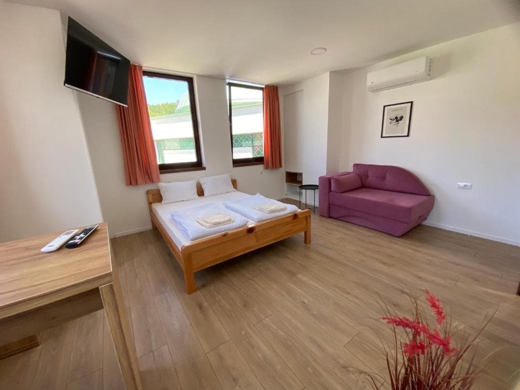 Double room with light wood bed, lounge seating, and windows with natural light.