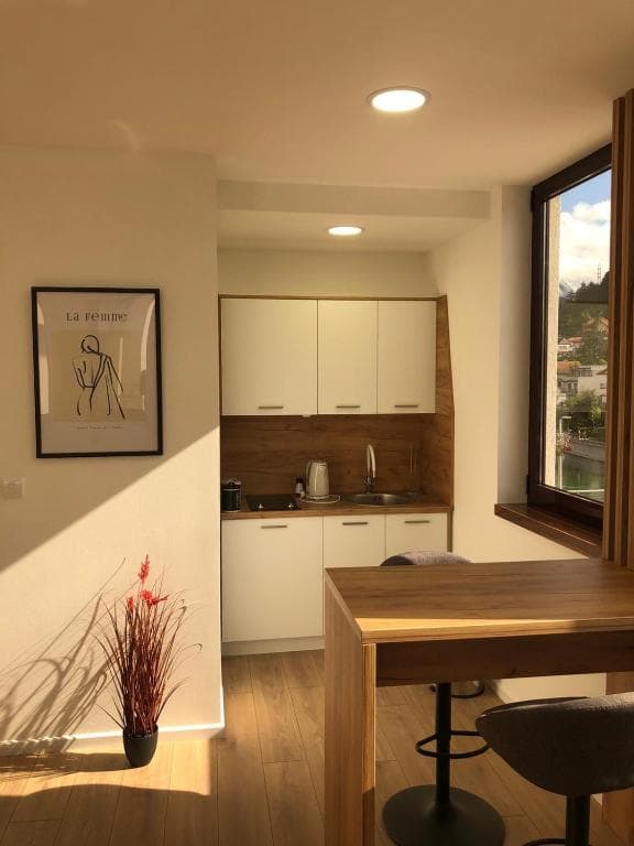 Modern kitchenette and bar-height dining area with wood surfaces and a window view over Konjic.
