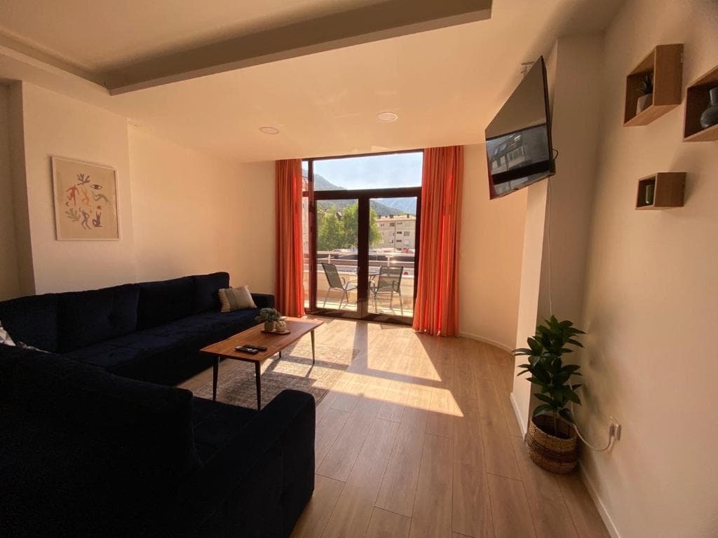 Bright living room with deep blue sectional, wood flooring, and glass doors opening to a balcony with a valley view.