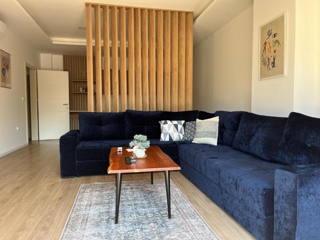 Living area with navy velvet sectional, live-edge coffee table, and wooden slat room divider.
