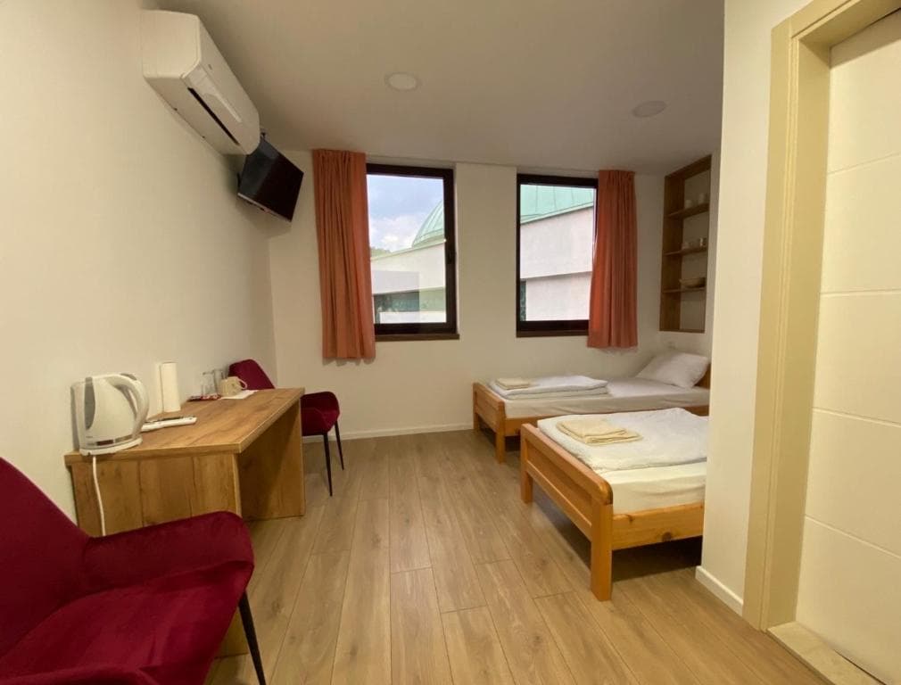 Twin room with two single beds, desk, and tall windows with warm curtains.